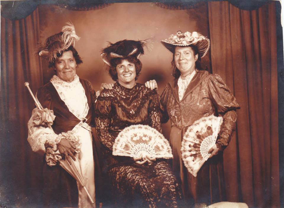 Mary Doan, Pamela Cloar, and Virginia Rogers dressed in vintage costumes with fans, posing for a fun old-timey photo