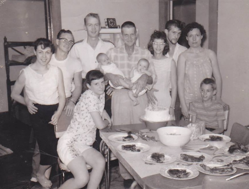Family photo with Elmer Doan holding twin babies, Mary Harris Doan, Jimmy Doan, Pam, Bobby Lee Kain, and other relatives gathered around a table with food and a cake