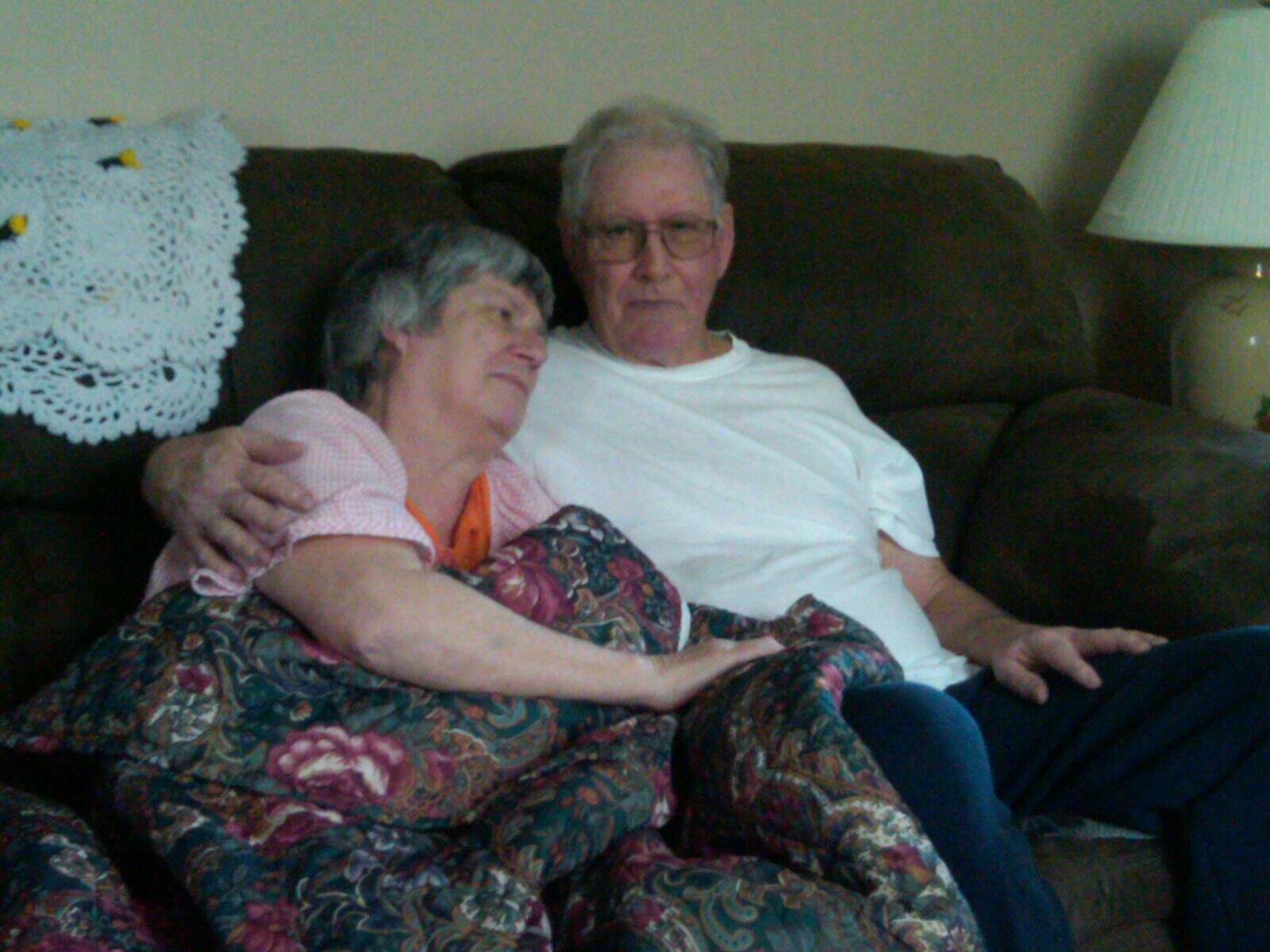 Virginia resting on Ishmael’s shoulder under a floral quilt